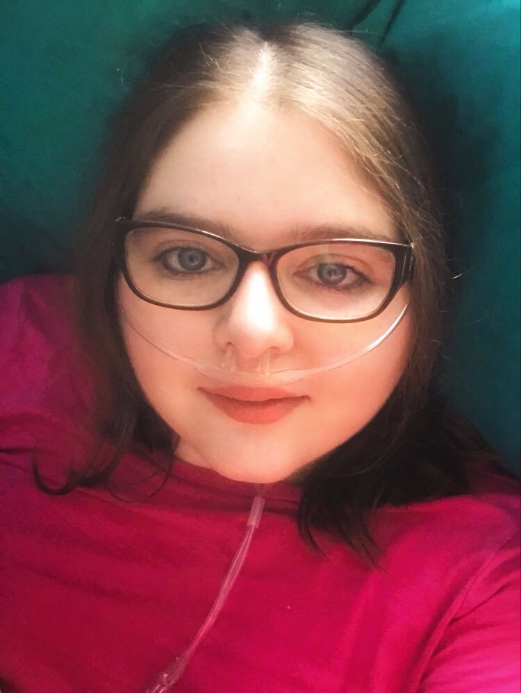 Kara Jane Spencer in a pink top. She wears glasses and has an oxygen nasal cannula